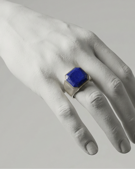Hand wearing a ring with a blue gemstone on a neutral background