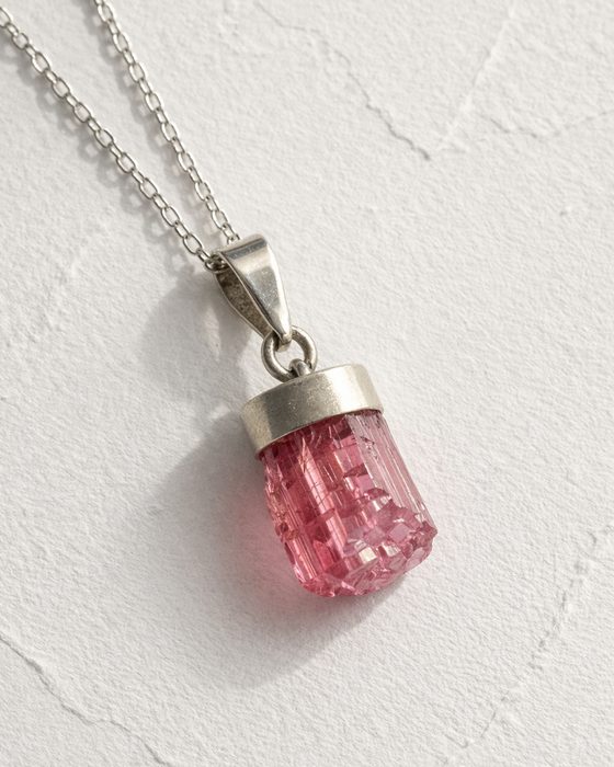 Pink crystal pendant on a silver chain against a white background