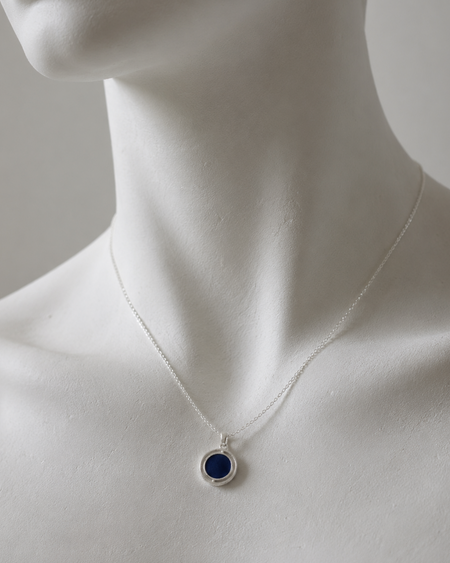 Mannequin wearing a necklace with a blue pendant on a neutral background