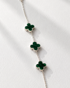 Silver bracelet with green clover-shaped charms on a white fabric background