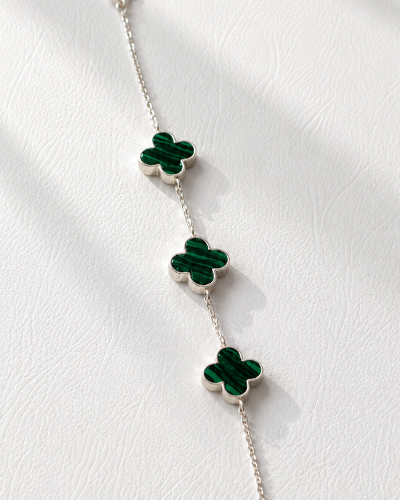 Silver bracelet with green clover-shaped charms on a white fabric background