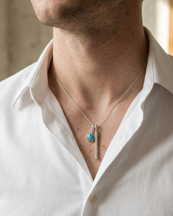 Man wearing a white shirt with a necklace featuring a turquoise pendant.