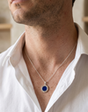 Man wearing a white shirt with a silver necklace featuring a blue pendant.