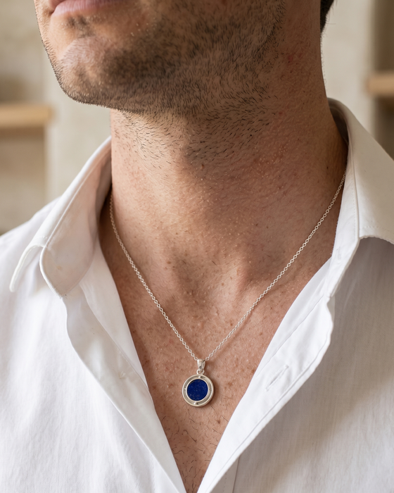 Man wearing a white shirt with a silver necklace featuring a blue pendant.