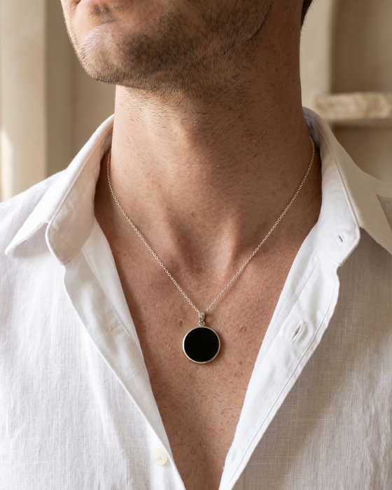 Man wearing a white shirt with a necklace featuring a black pendant.