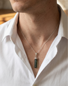 Man wearing a white shirt with a green pendant necklace.