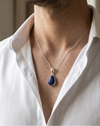 Man wearing a white shirt with a necklace featuring a blue pendant.
