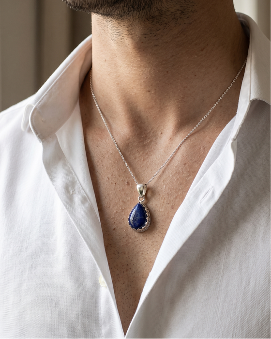 Man wearing a white shirt with a necklace featuring a blue pendant.