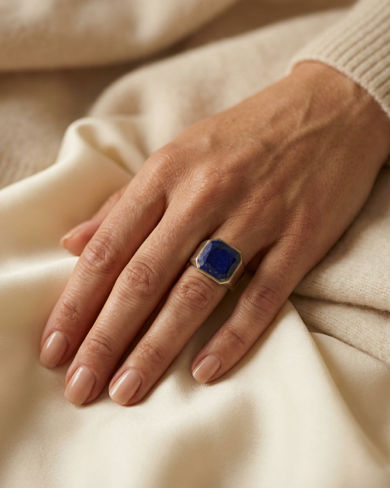 Hand wearing a blue ring on a beige sweater