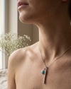 Necklace with a turquoise bead and silver chain worn by a person indoors.