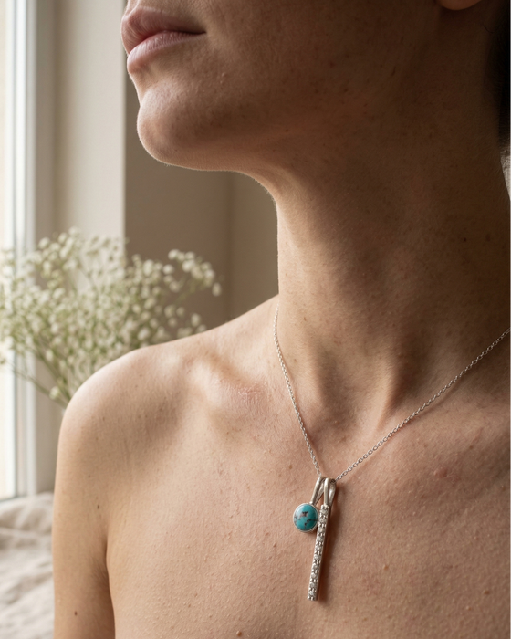 Necklace with a turquoise bead and silver chain worn by a person indoors.