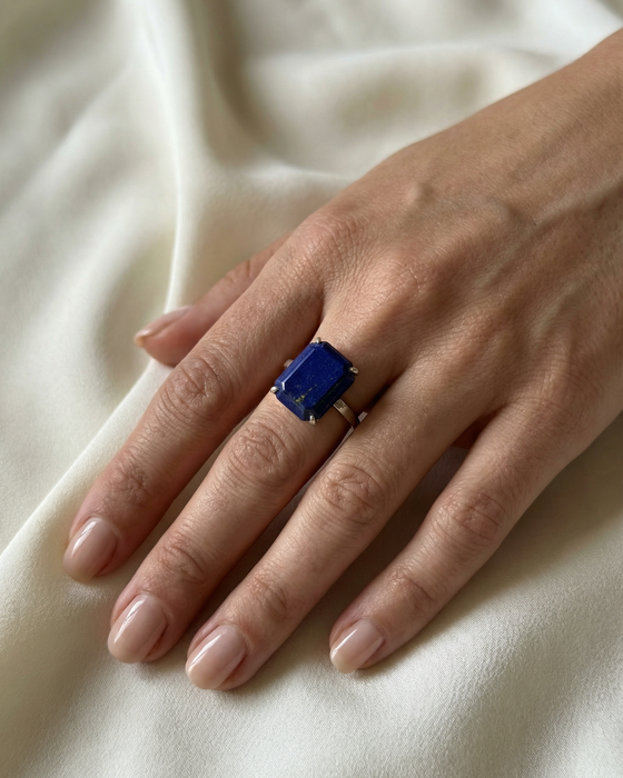 Hand wearing a ring with a blue gemstone on a white fabric background