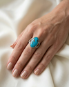 Hand wearing a turquoise ring on a white fabric background