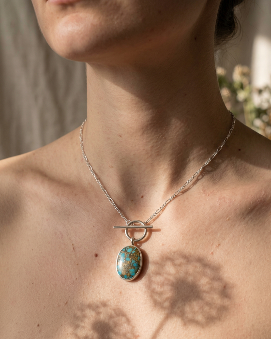 Necklace with a turquoise pendant worn by a person, with a blurred background.