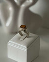 Silver ring with a brown gemstone on a white pedestal