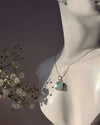 Necklace with a pendant on a mannequin bust, with flowers to the side.
