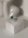 Silver ring with a blue gemstone on a white stand