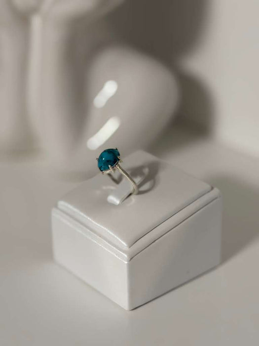 Silver ring with a blue gemstone on a white stand