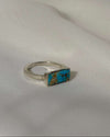 Silver ring with a rectangular turquoise stone on a white fabric background