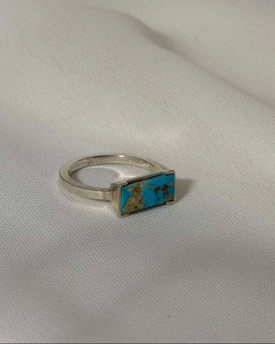 Silver ring with a rectangular turquoise stone on a white fabric background
