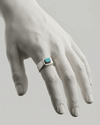 Hand wearing a silver ring with a turquoise stone on a light gray background