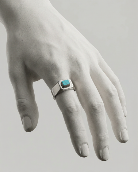 Hand wearing a silver ring with a turquoise stone on a light gray background