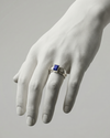 White marble hand wearing a silver ring with a blue gemstone on a gray background
