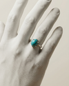 Turquoise ring on a white hand against a beige background