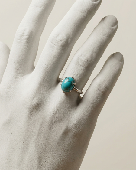 Turquoise ring on a white hand against a beige background
