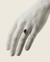 Hand wearing a ring with a blue gemstone on a neutral background