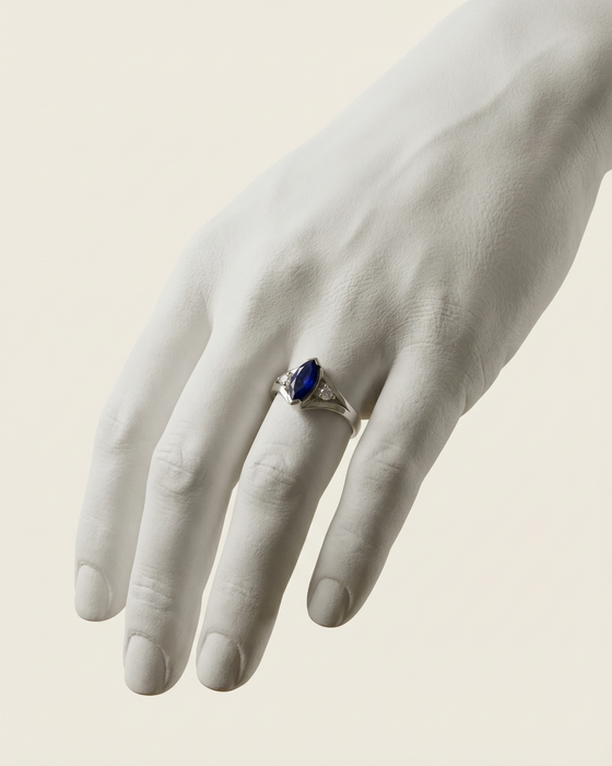 Hand wearing a ring with a blue gemstone on a neutral background