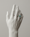 White marble hand wearing a ring with a blue gemstone on a neutral background