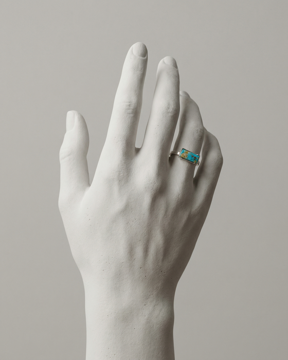 White marble hand wearing a ring with a blue gemstone on a neutral background
