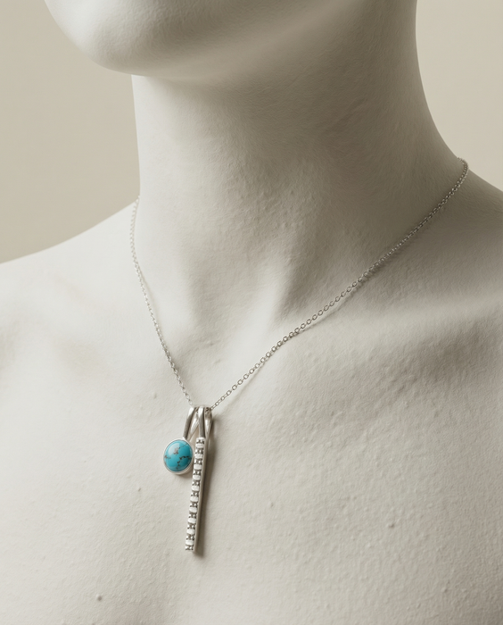 Necklace with a turquoise pendant and silver chain on a mannequin.